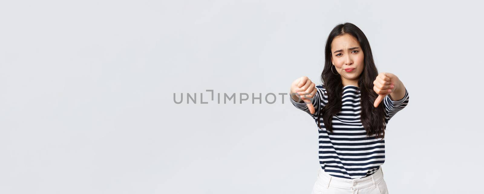 Lifestyle, beauty and fashion, people emotions concept. Judgemental disappointed asian woman showing negative opinion, make thumbs-down and smirk unsatisfied, rating bad product by Benzoix