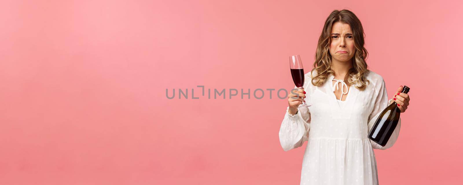 Holidays, spring and party concept. Portrait of upset and whining young blond woman being cheated trying to ease pain with alcohol, holding glass wine and bottle, grimacing want cry, complaining by Benzoix