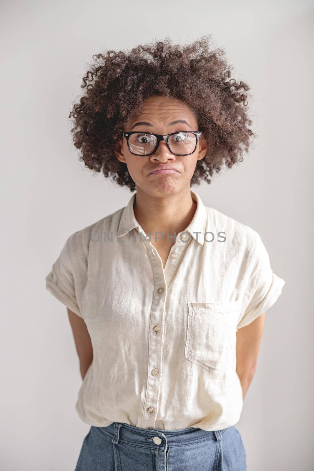 Portrait of confused African American woman in glasses posing in studio, isolated on grey background