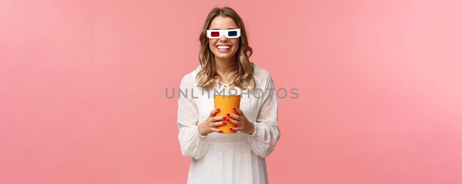 Leisure, going-out and spring concept. Portrait of happy carefree blond girl in white dress enjoying watching movie in 3d, wearing glasses eating popcorn and smiling, attend cinema, pink background by Benzoix