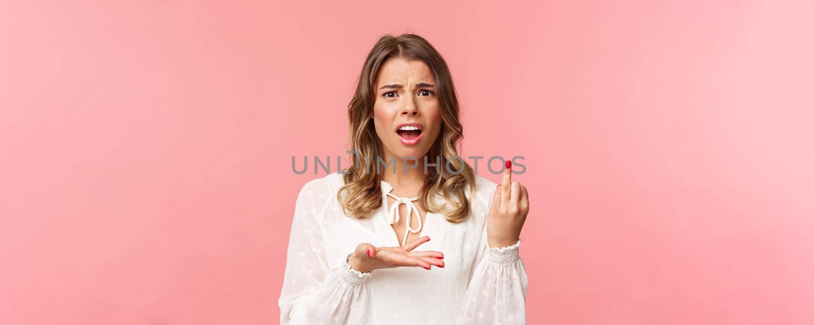 Close-up portrait of frustrated pissed-off, complaining beautiful girl tired of waiting for proposal, pointing at ring finger with bothered grimace, standing pink background disappointed.