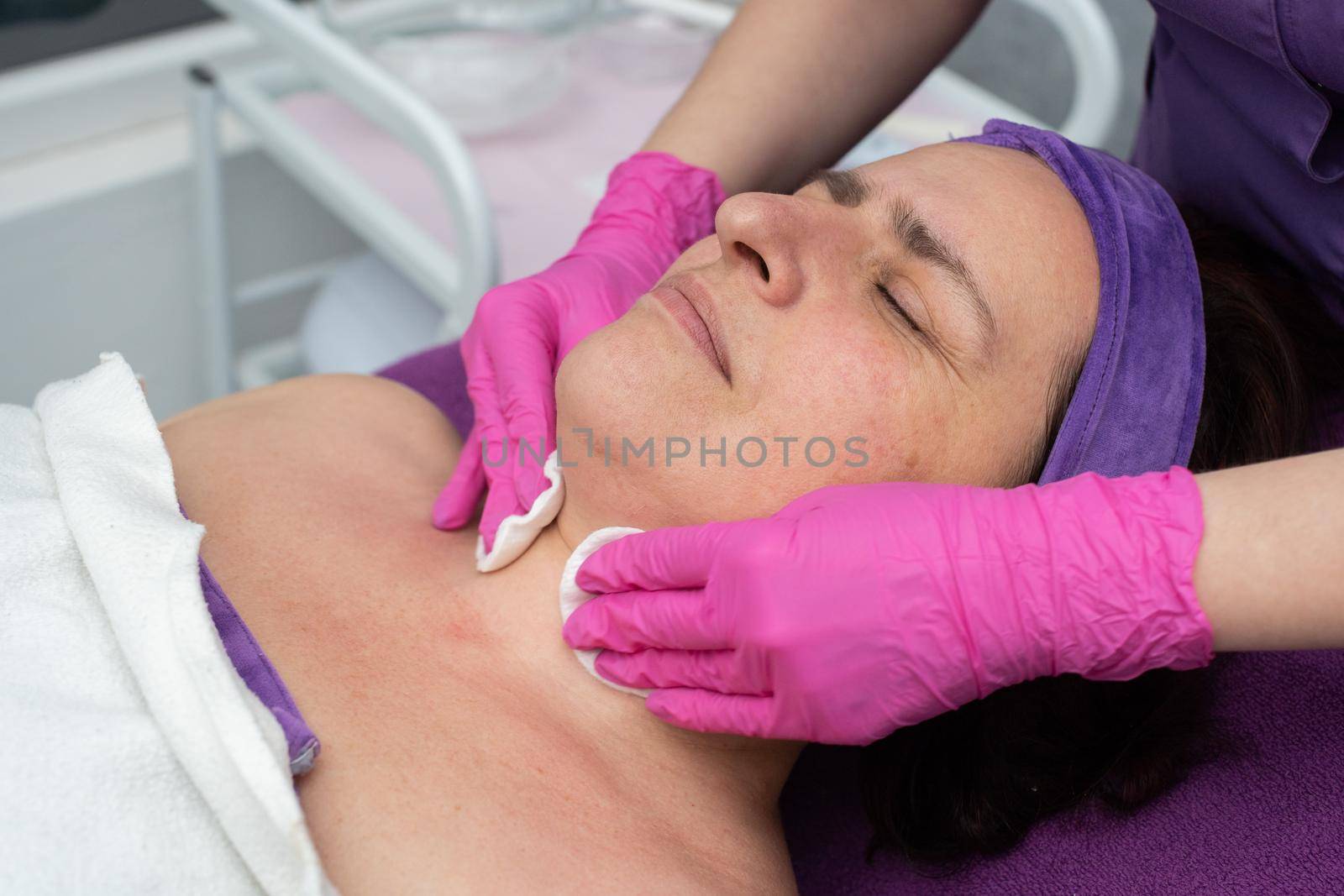A professional beautician cleans the skin on the face with cosmetic pads for a 50-year-old woman