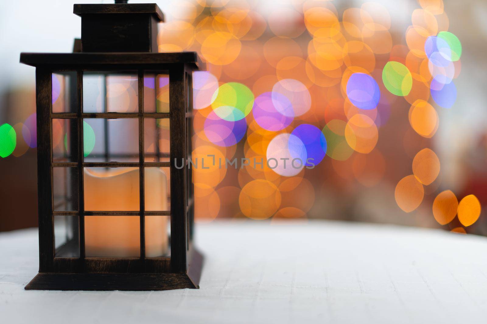 Rectangular old hand lantern with a glowing candle in the center. In the distance a blurred background created from the bokeh of glowing Christmas tree lights