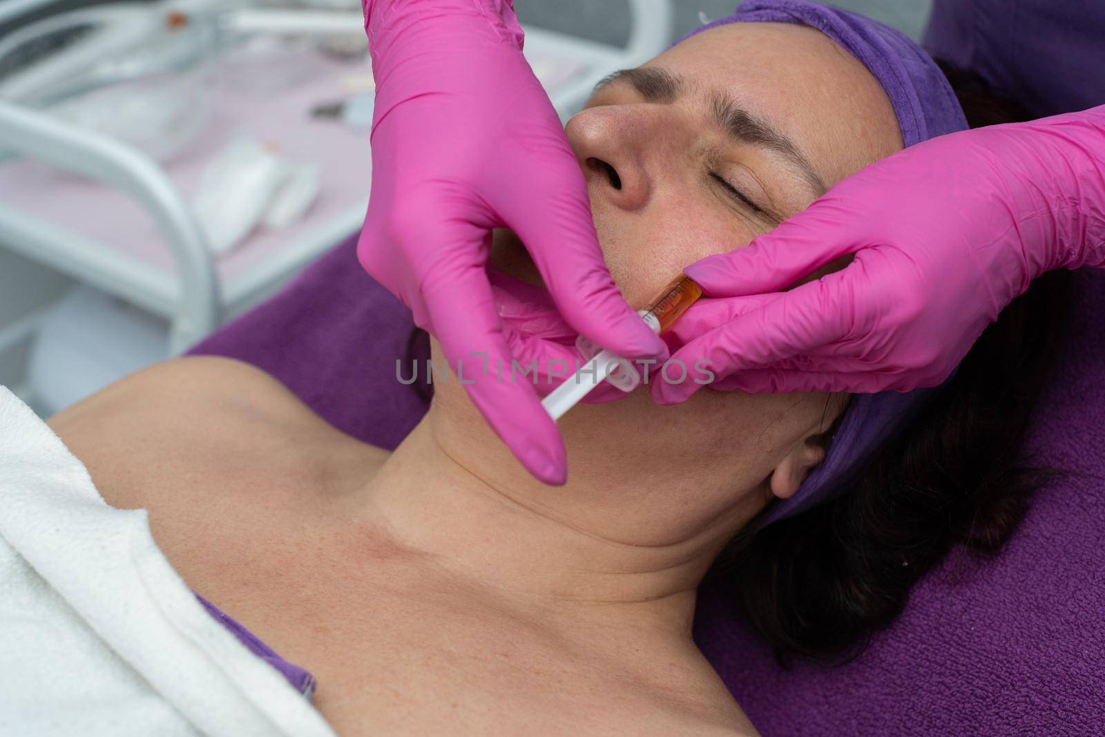 The beautician squeezes the brightening serum into the skin of the client's face from the syringe to reduce redness and wrinkles