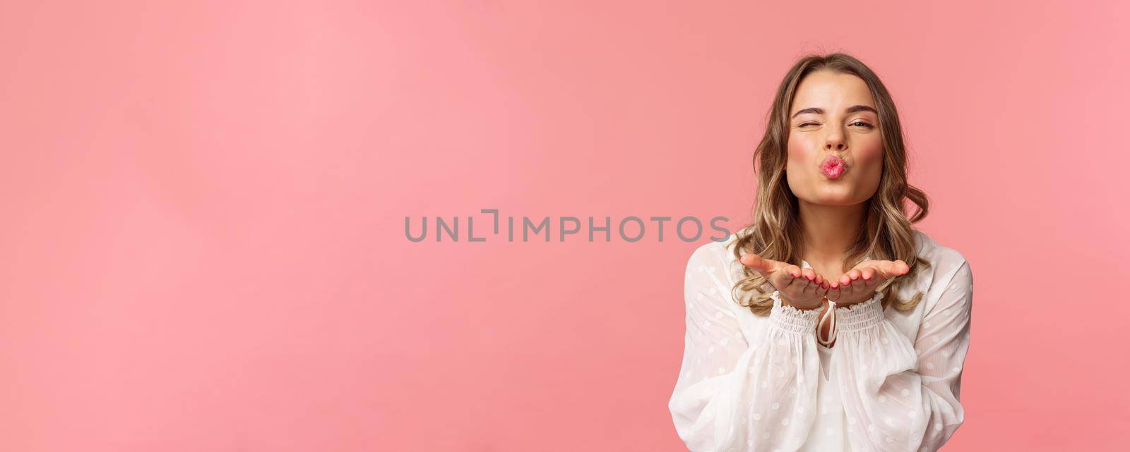 Close-up portrait of lovely feminine girlfriend enjoying spring fine day, sending air kiss at camera, winking and folding lips in mwah, hold hands near mouth, pink background by Benzoix