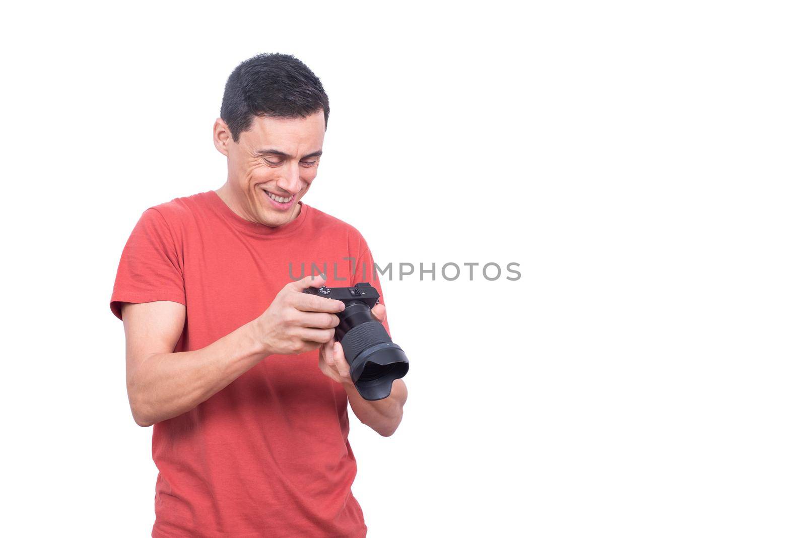 Delighted male photographer looking at modern professional photo camera with photos while standing in light studio isolated on white background