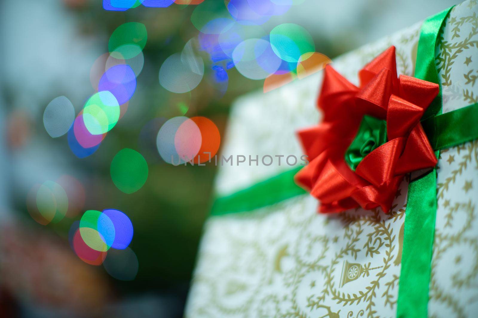 A large red bow on a Christmas gift. A decorative box with a Christmas gift in the background with cork lights.