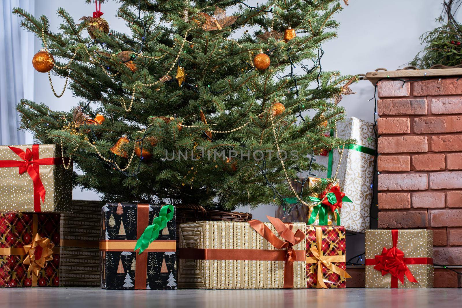 The holiday gifts lie under a decorated spruce tree in the large living room of the house. Family holidays full of joy and cordiality at Christmas.