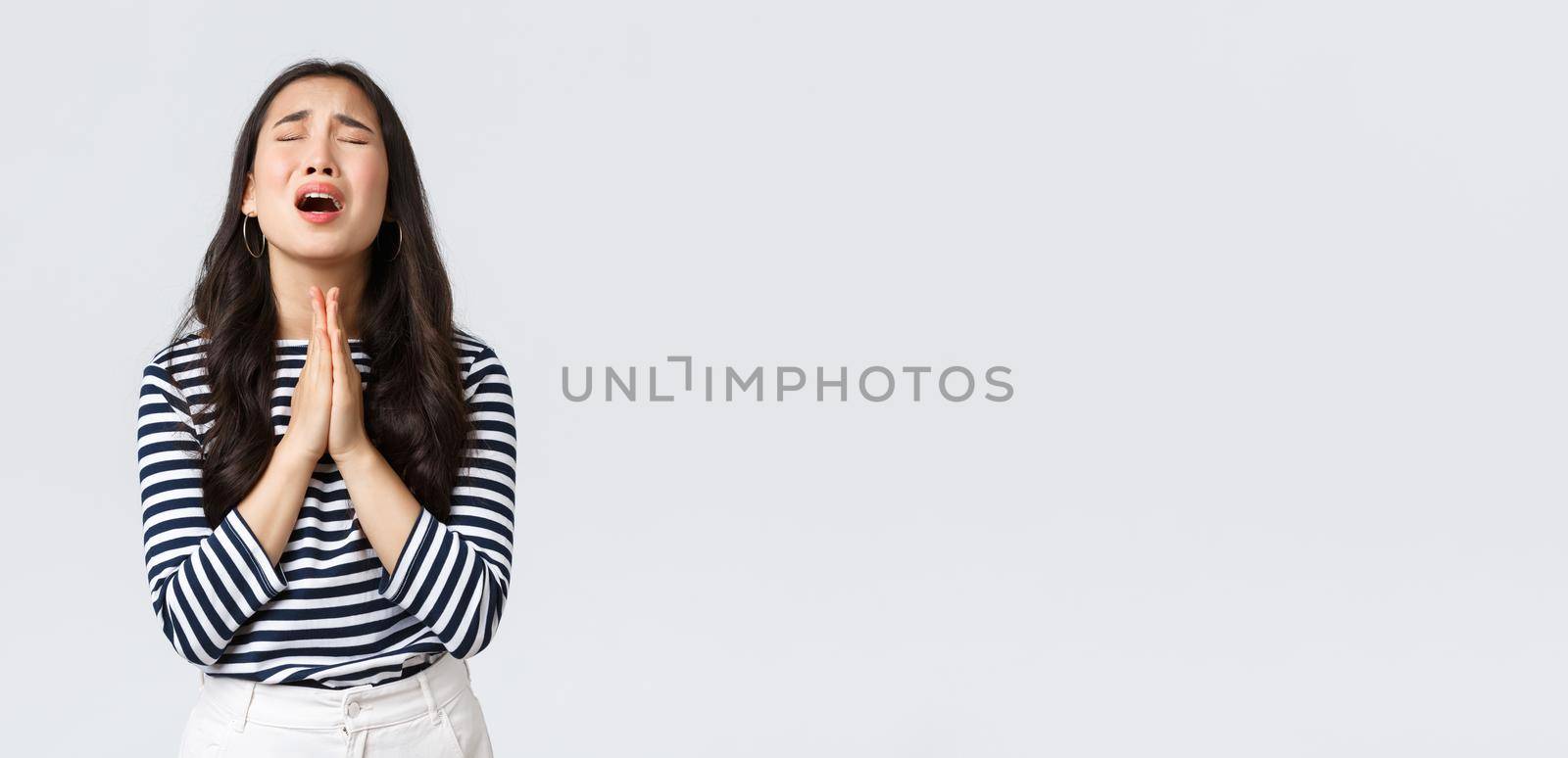 Lifestyle, people emotions and casual concept. Desperate hopeful asian girl making wish, close eyes and hold hands in pray, pleading god to have something, making wishful face, white background.