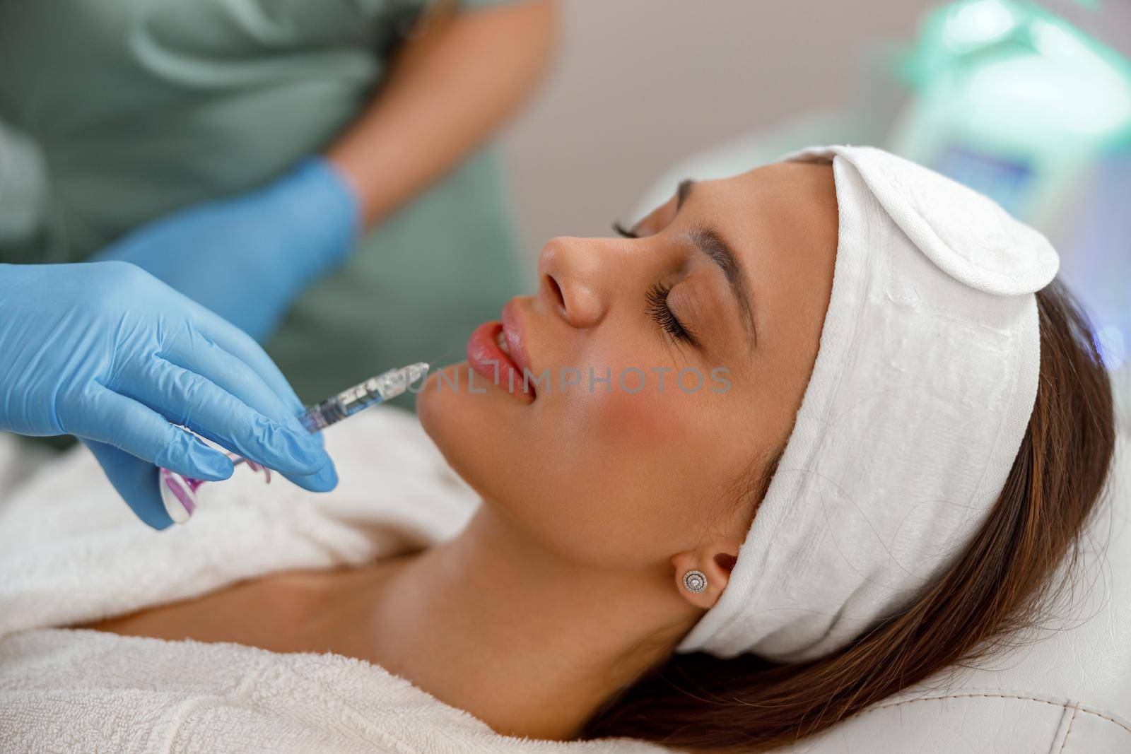 Relaxed young woman getting hyaluronic acid injections in lips at beauty salon. Cosmetology