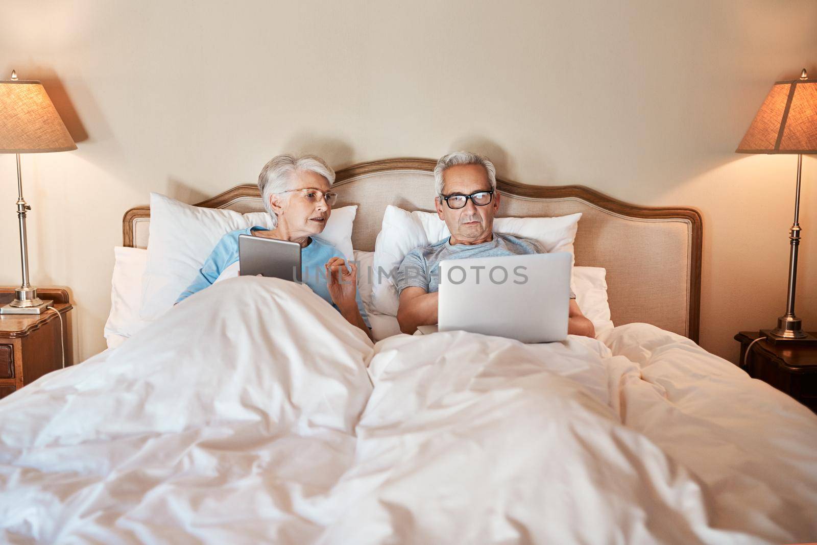 Cropped shot of a senior couple sitting in bed together and using technology in a nursing home.