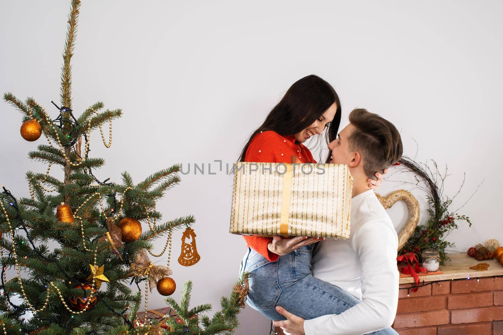 The fiance lifted his partner up in a fit of joy. Lovers flirt in a decorated living room at home. December Christian holidays.