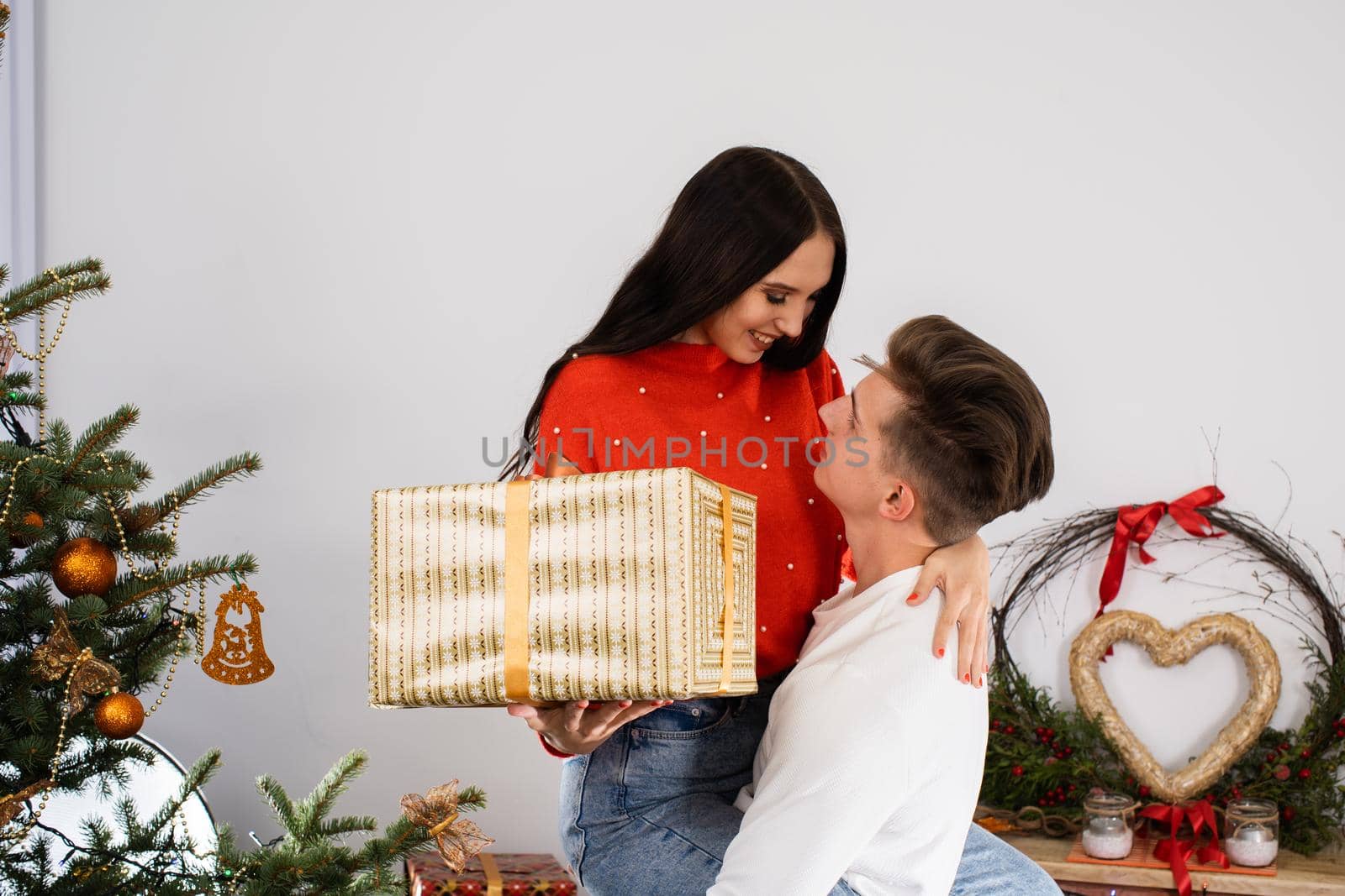 The fiance lifted his partner up in a fit of joy. Lovers flirt in a decorated living room at home. December Christian holidays.