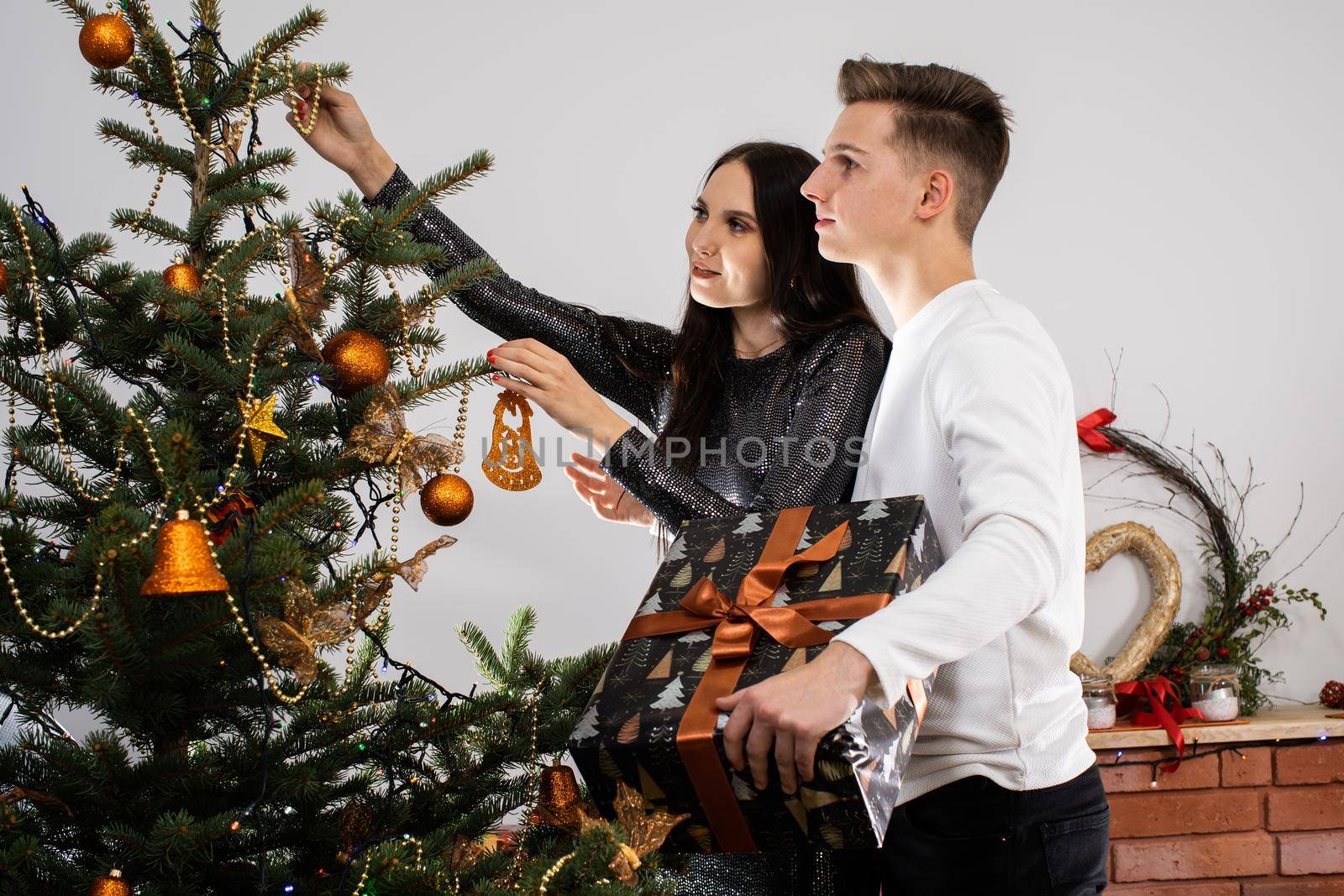 Couple in love while decorating the Christmas tree for Christmas. Smiling young people. Shiny black dress.
