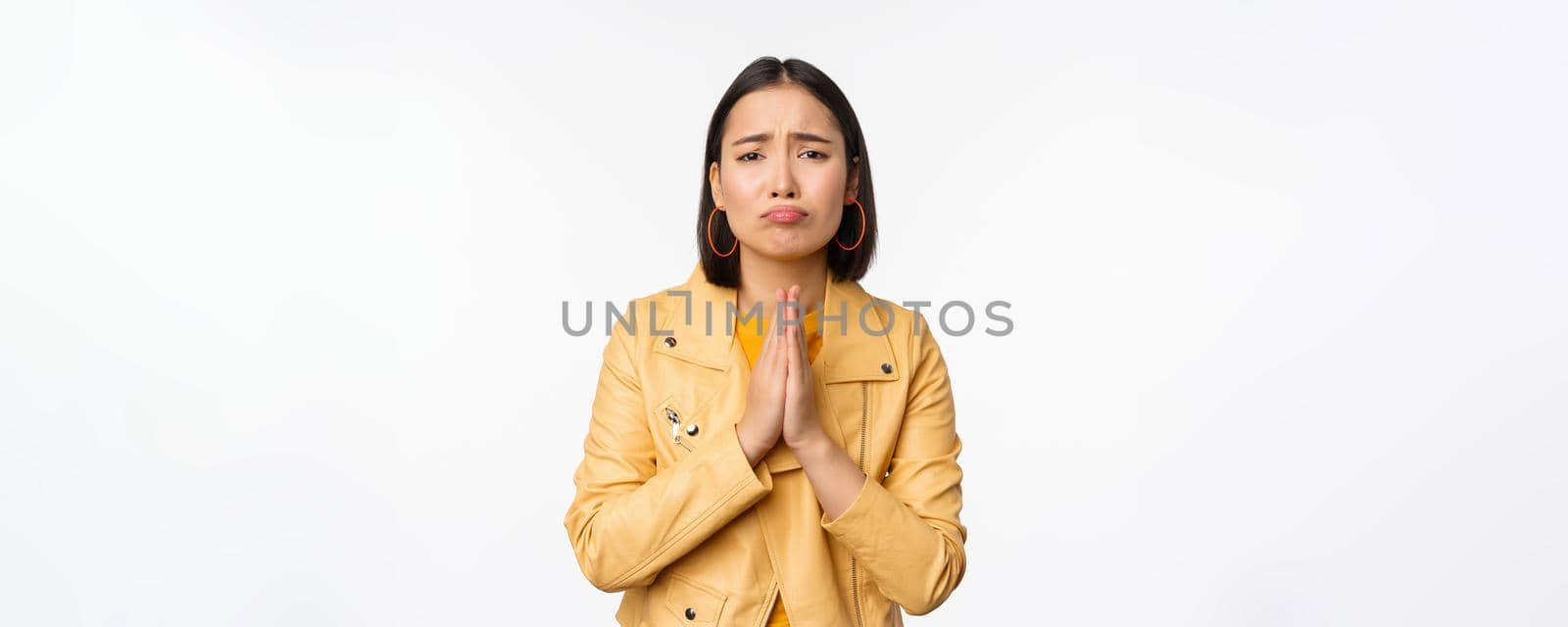 Image of hopeless asian woman begging, pleading, say sorry, looking distressed and miserable, standing over white background.