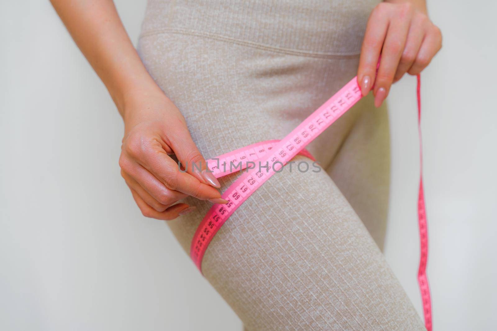 Cropped view of slim woman measuring her leg with tape measure at home, close-up. An unrecognizable European woman checks the result of a weight loss diet or liposuction indoors. Healthy lifestyle