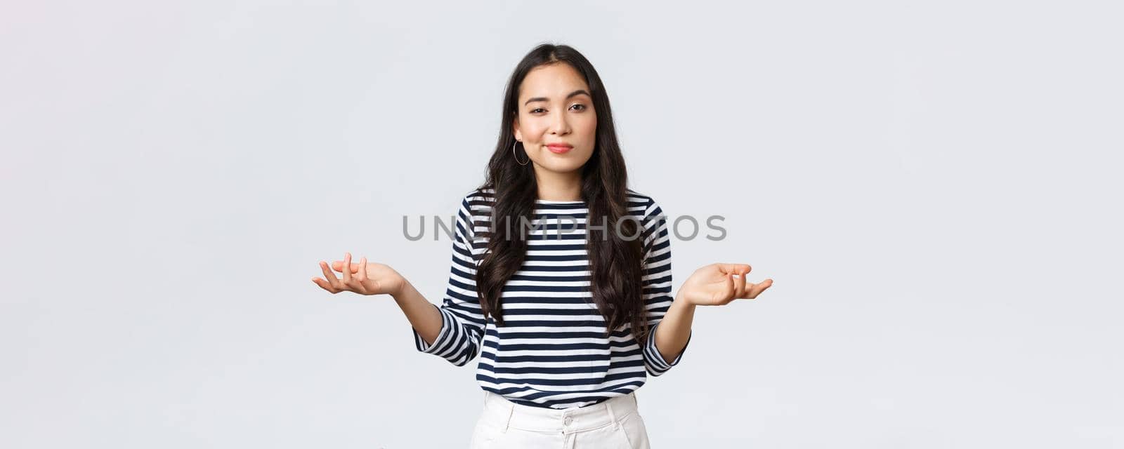 Lifestyle, beauty and fashion, people emotions concept. Clueless and unbothered asian woman shrugging with hands spread sideways and unaware smirk, standing white background.