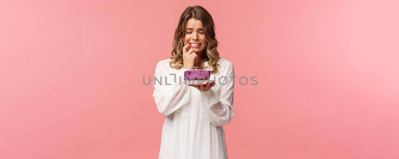 Holidays, spring and party concept. Portrait of nervous blond girl on diet, biting lip cant resist temptation to eat delicious cake, looking at dessert with hesitant expression, grimacing worried by Benzoix