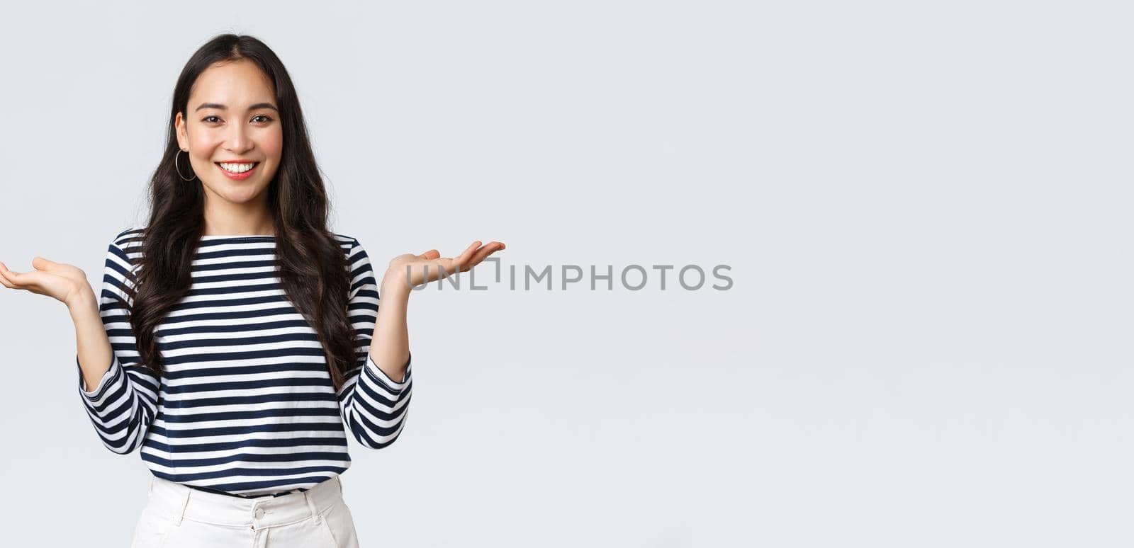 Lifestyle, people emotions and casual concept. Cute smiling asian woman introduce two products, hold hands sideways as if demonstrating products on palms, standing white background.