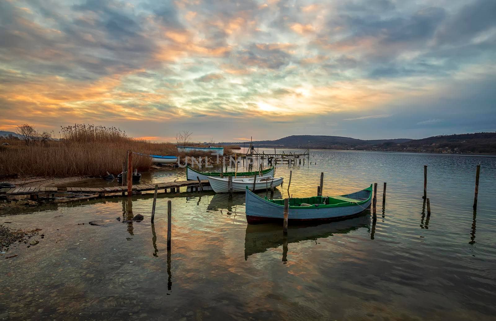 The tranquil afternoon on a lake with a wooden pier and boats at colorful sky.