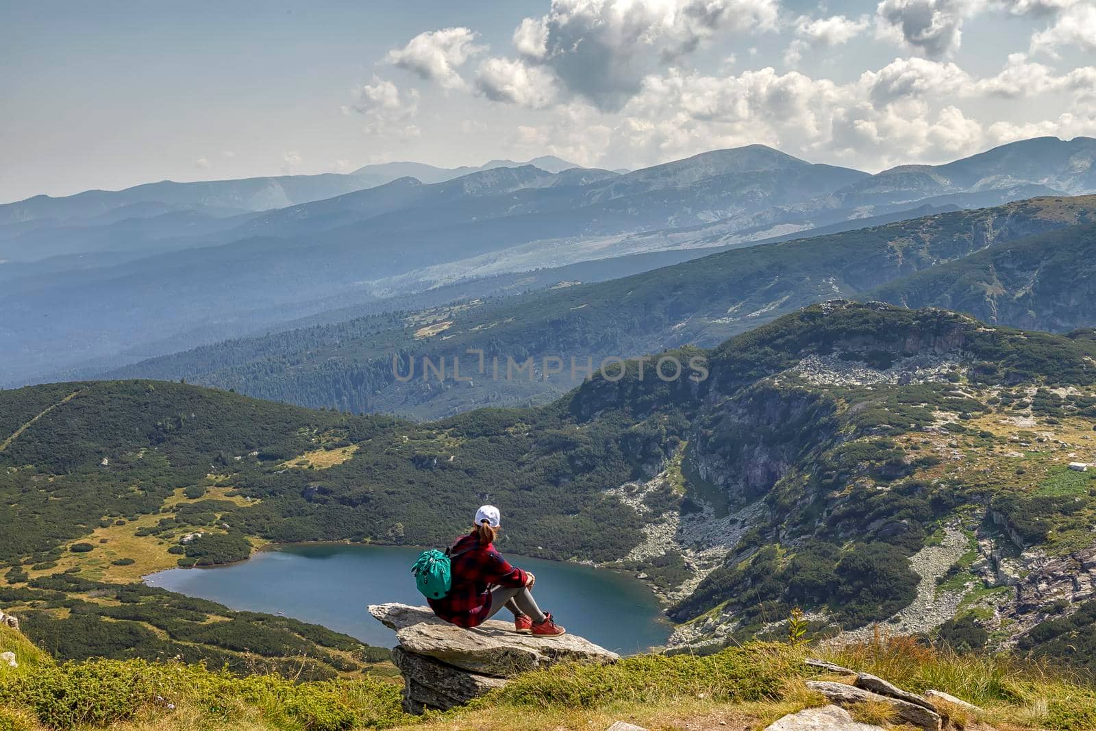 A young girl enjoys a beautiful view sitting on the rock from the top. Travel in the mountains.