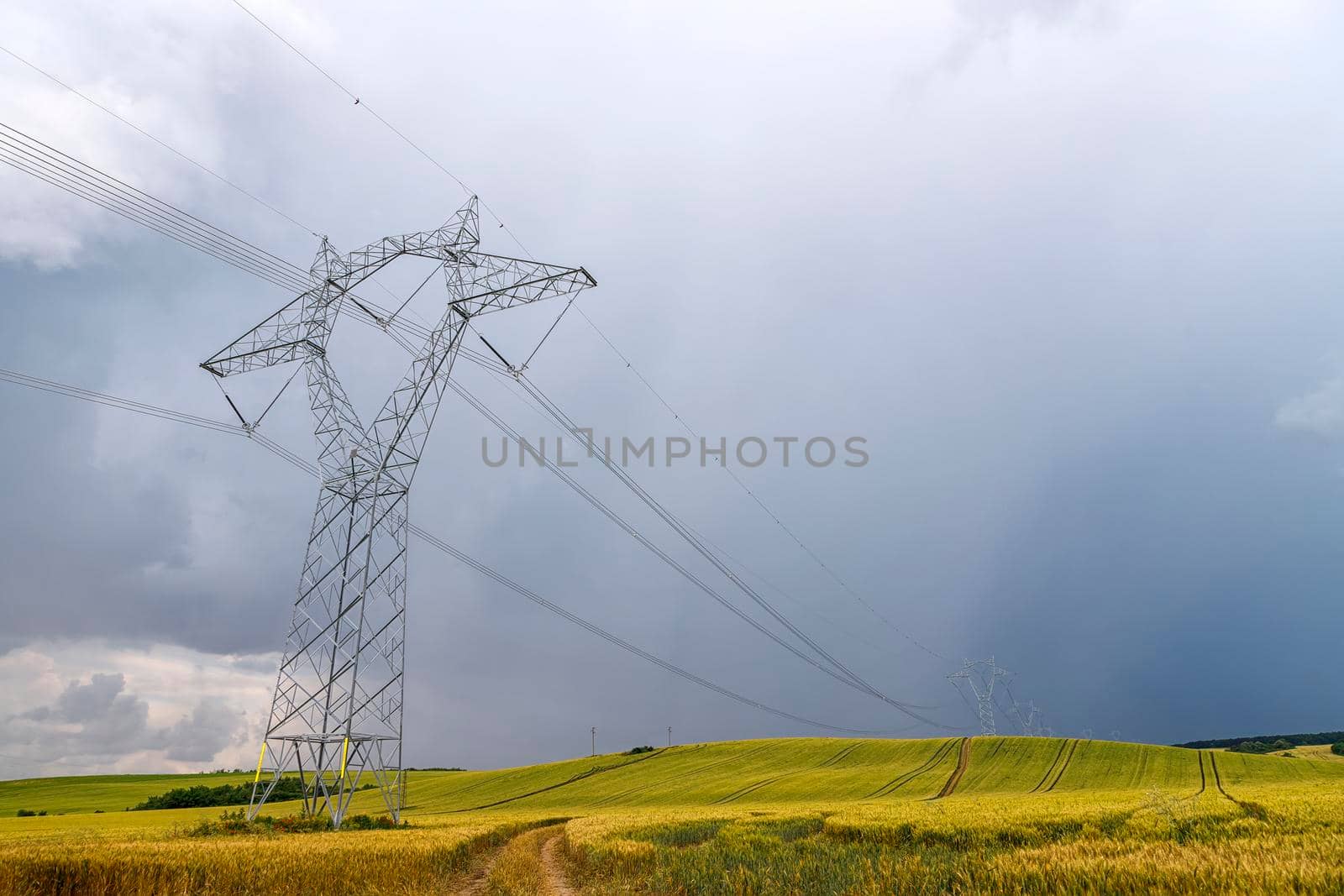 High voltage electric pole and transmission lines over golden wheat field with road