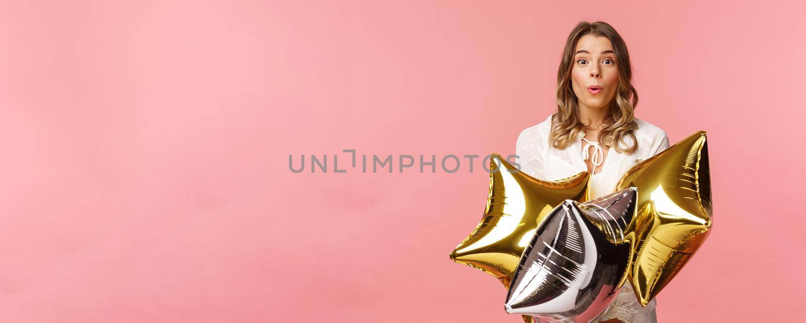 Holidays, celebration and women concept. Portrait of surprised happy attractive blond girl in white lovely dress, fold lips say wow being impressed with friends made b-day party, hold balloons by Benzoix