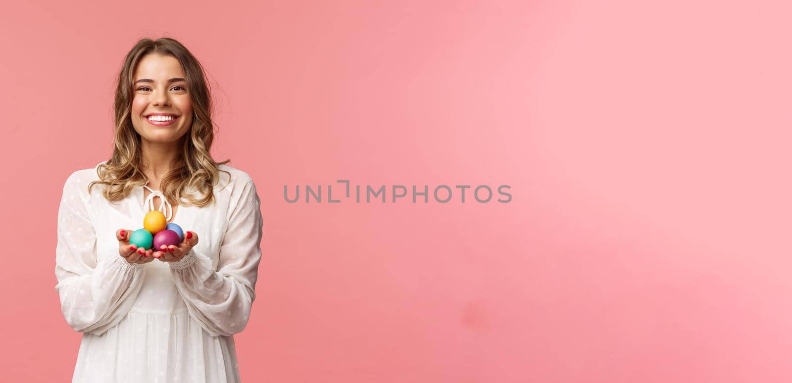 Holidays, spring and party concept. Portrait of tender, lovely blonde girl in white dress, holding Easter painted eggs, celebrating orthodox day, smiling cheerful share positivity, pink background by Benzoix