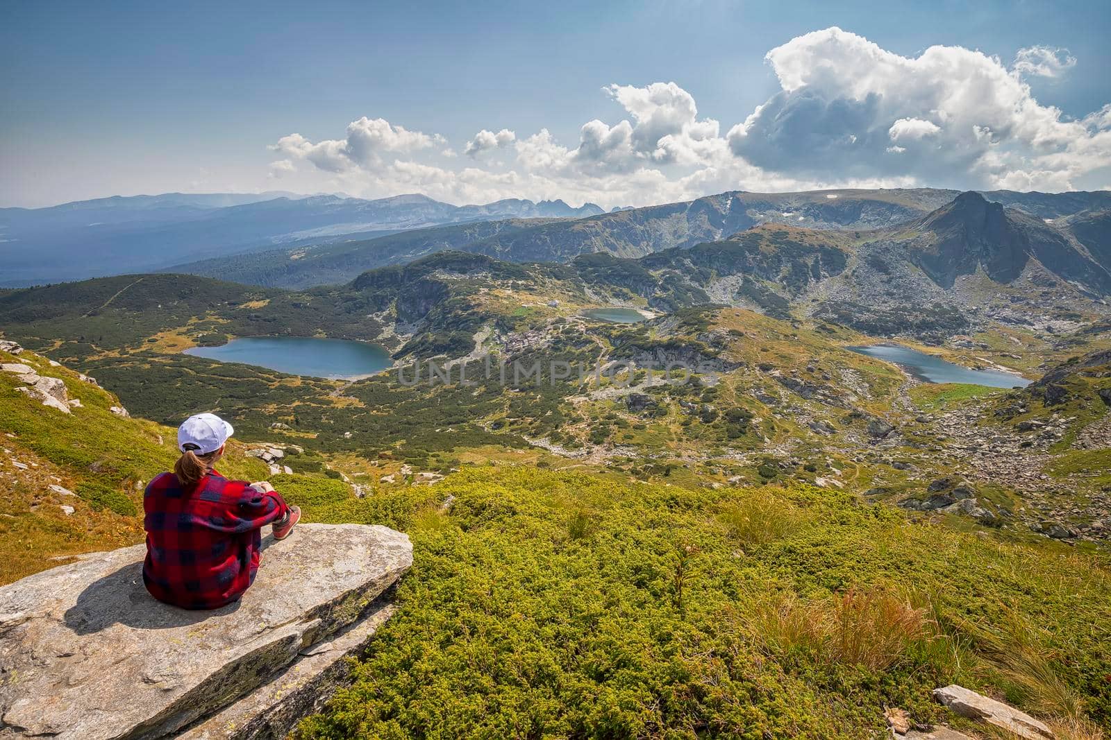 A young girl enjoys a beautiful view sitting on the rock from the top. Travel in the mountains.