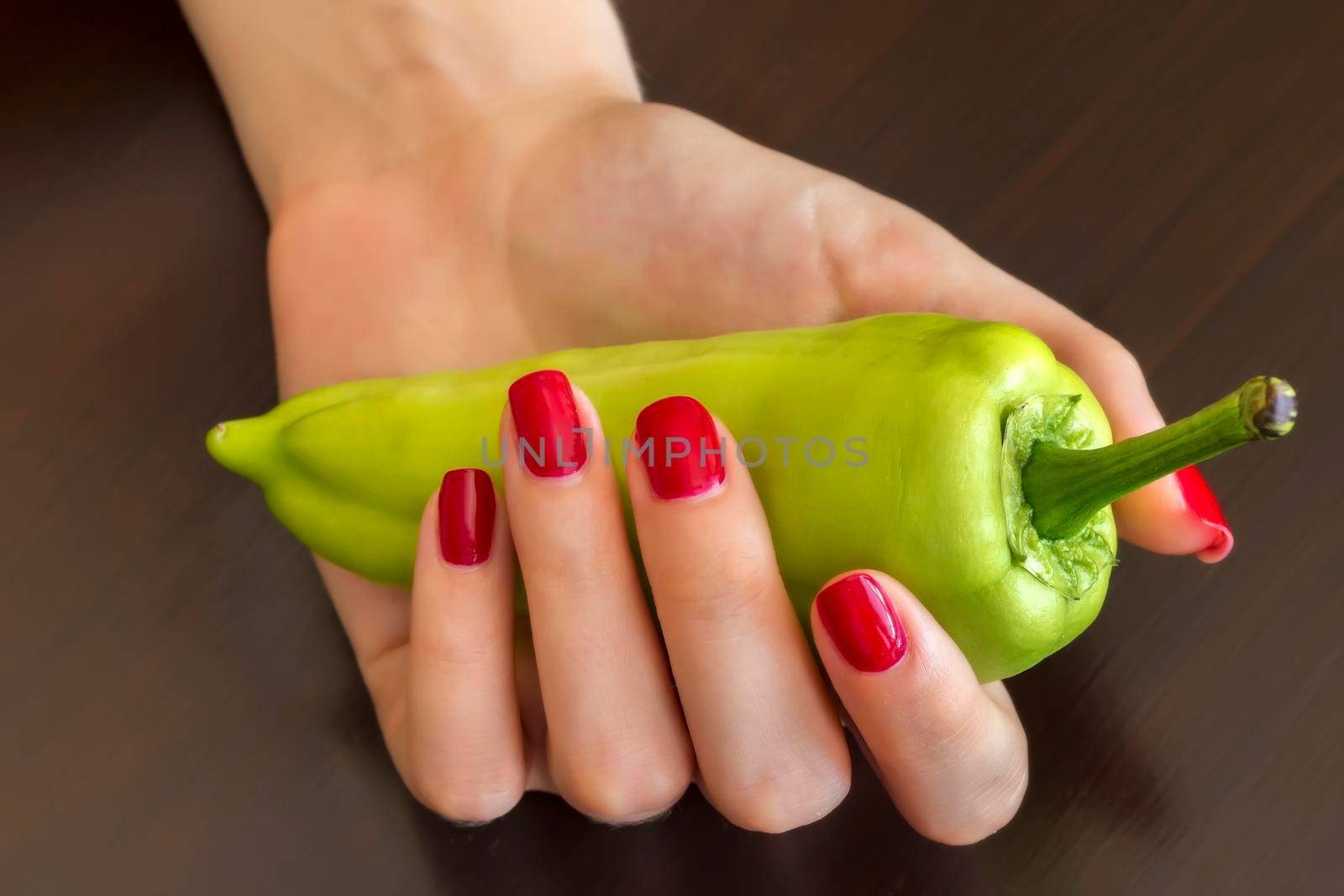 Beautiful female hand with a red nails holding green pepper. 