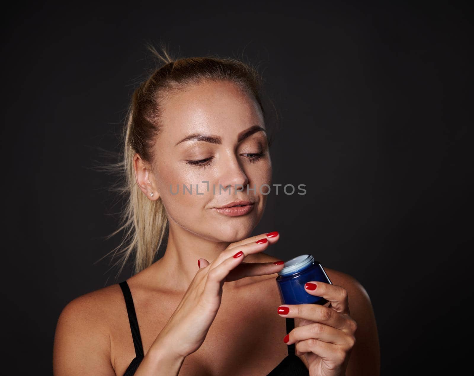 Closeup stunning beautiful middle aged European blonde woman applying face moisturizer, smoothing serum, taking care of facial skin. Cosmetic procedures against wrinkles, spa, wellness, youth concept by artgf