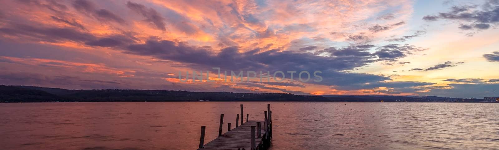Banner of colorful sunset at a lake coast at a wooden pier.