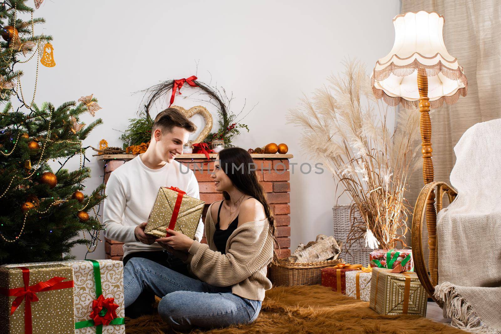 Two lovers are sitting by the Christmas tree on Christmas. Decorated Christmas tree and fireplace in the living room at home.