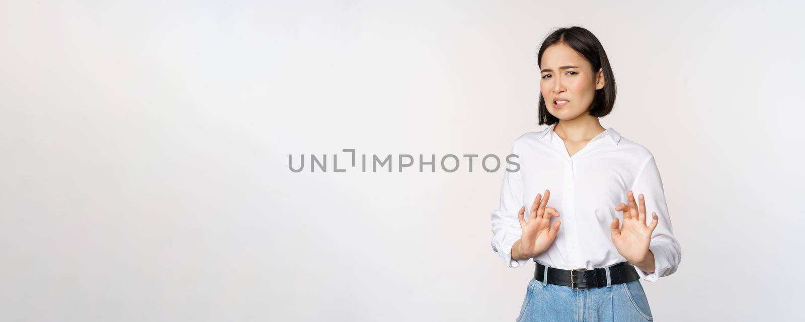 No thank you. Young disgusted asian woman declining proposal, shaking hands and step back, looking with dislike, rejecting offer, standing over white background.