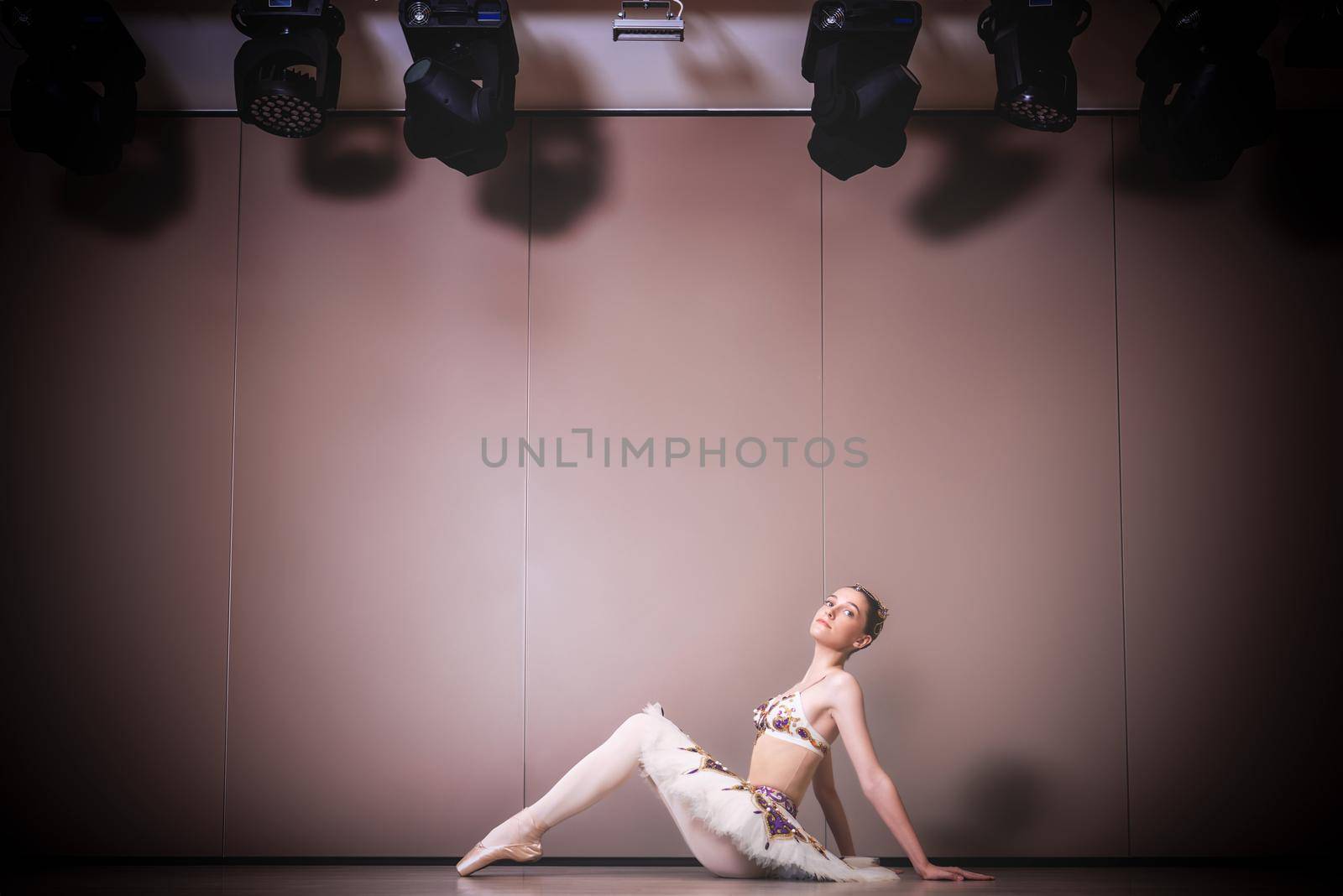 young beautiful graceful caucasian ballerina practice ballet positions in tutu skirt. Classical Ballet dancer sitting on the floor in the studio
