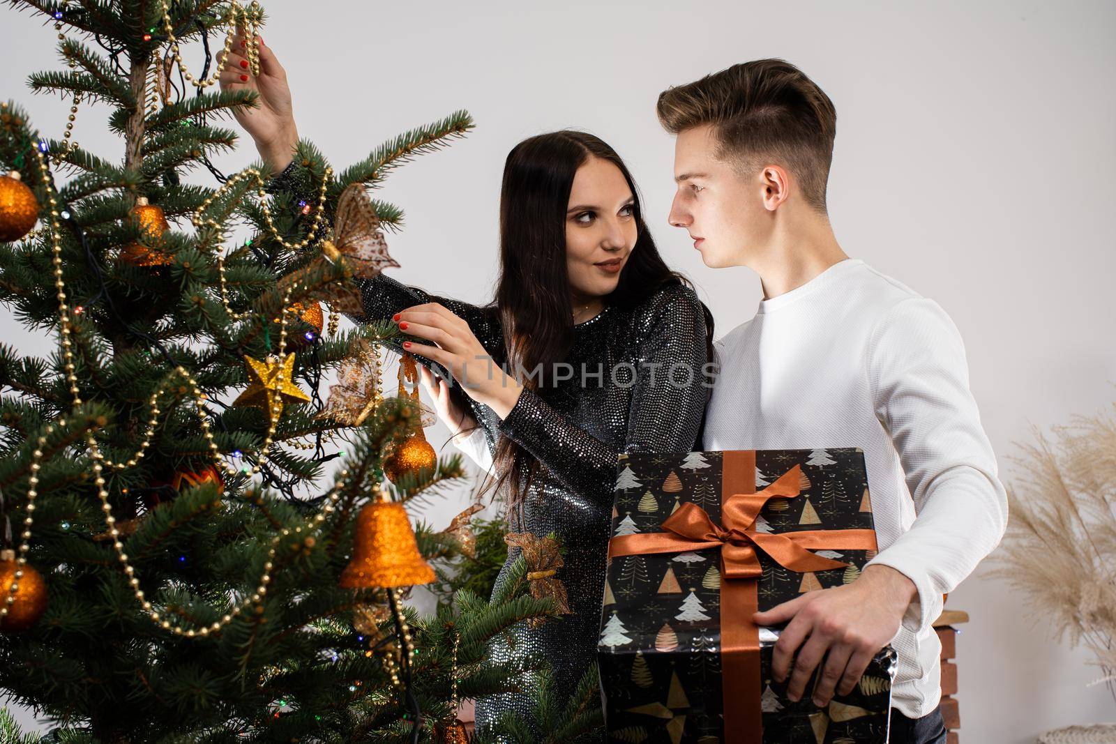 Couple in love while decorating the Christmas tree for Christmas. Smiling young people. Shiny black dress.