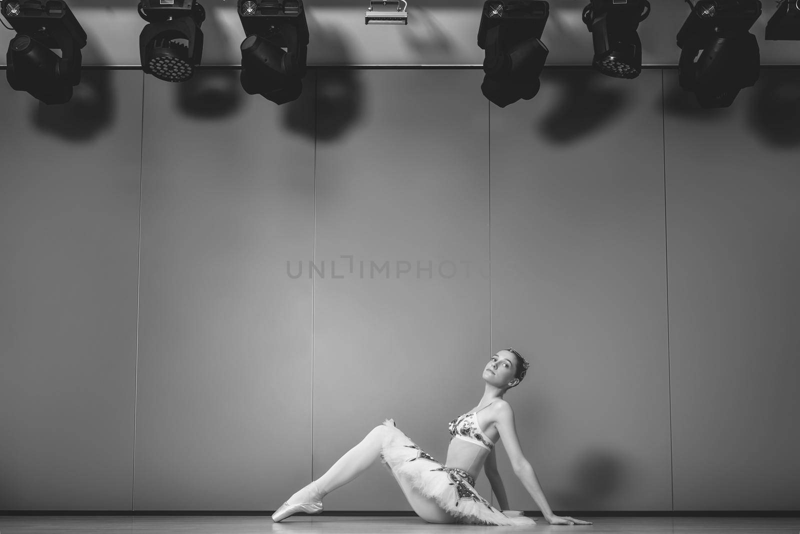 young beautiful graceful caucasian ballerina practice ballet positions in tutu skirt. Classical Ballet dancer sitting on the floor in the ballet studio. black and white filter by Nickstock
