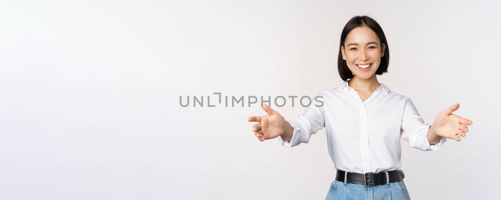 Image of smiling asian woman welcoming guests clients, businesswoman stretching out open hands, greeting, standing over white background.