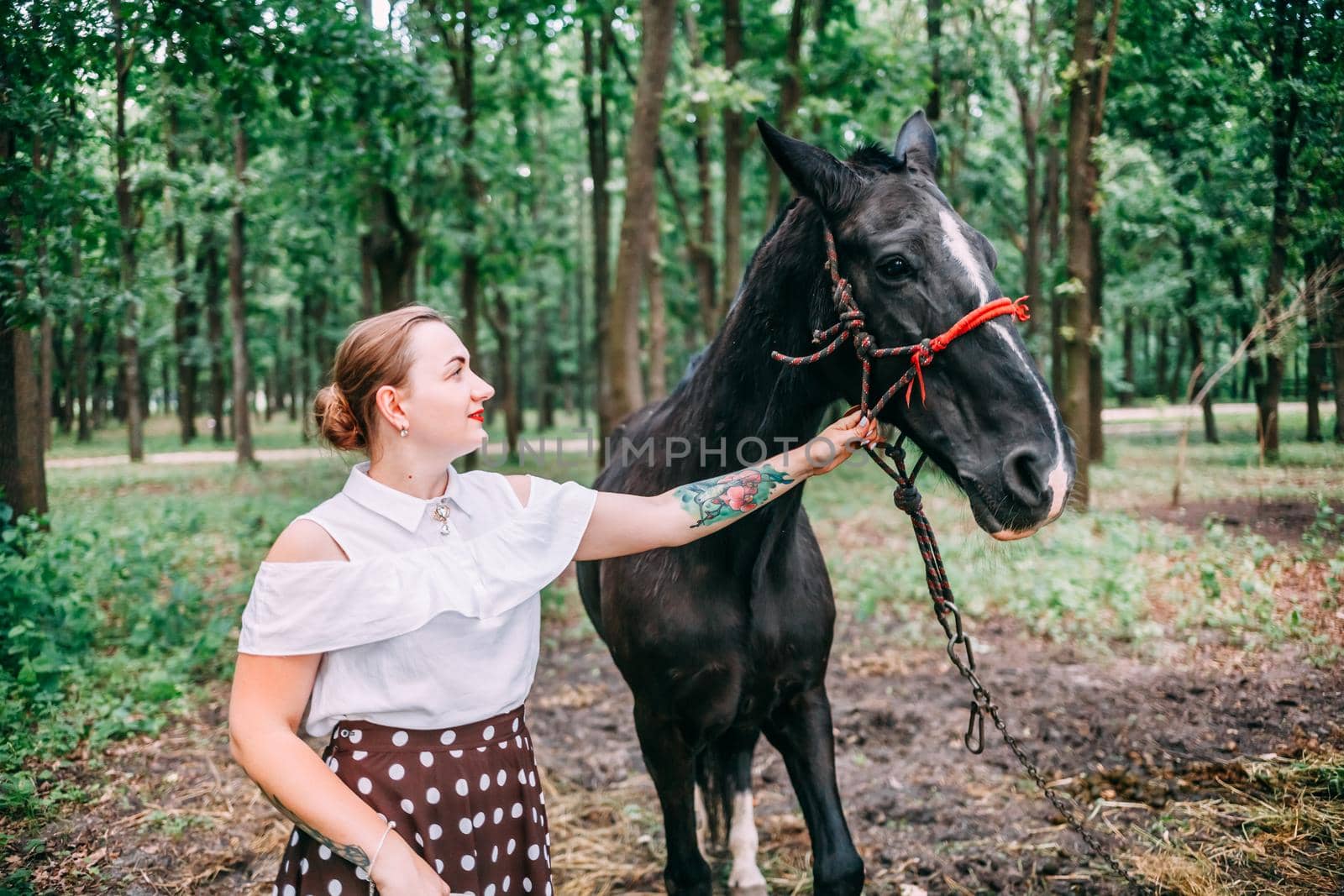 photo of a young smiling blonde, in a white blouse and skirt, with a horse, in a summer forest.