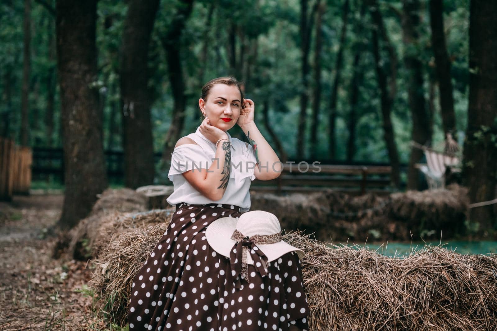 photo of a young smiling blonde, in a white blouse and skirt, on the hay in a summer forest.