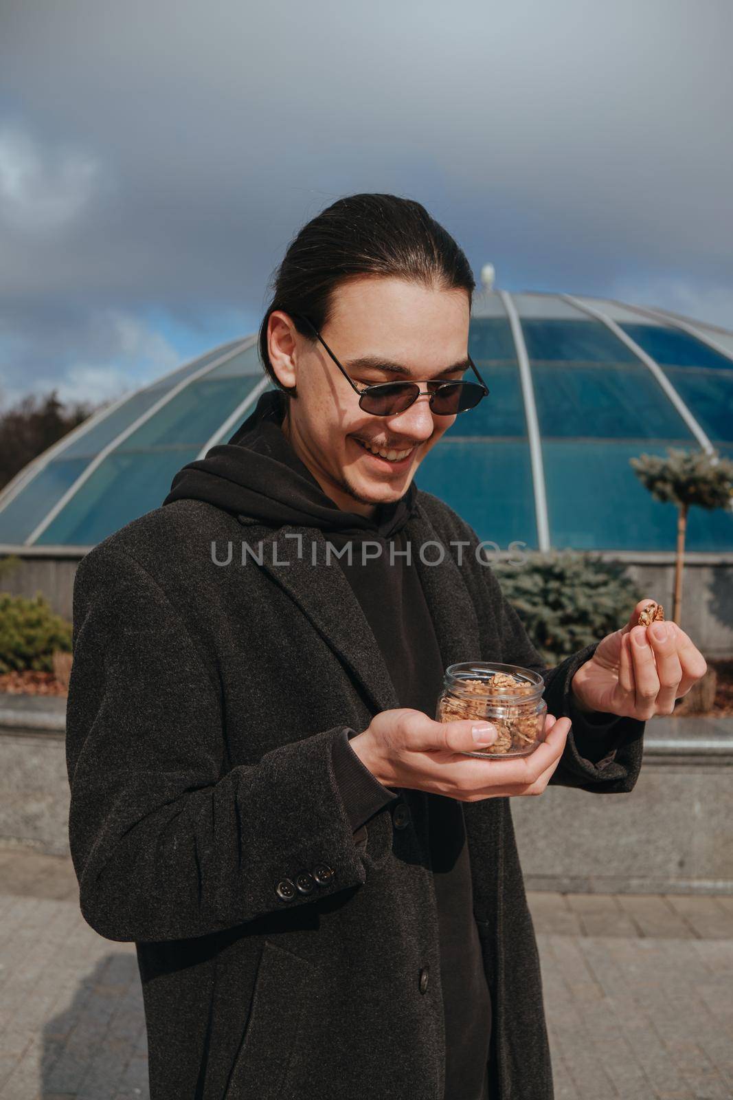 Young gay hipster eating peanuts at the street smiling happy sunglasses. Healthy lifestyle