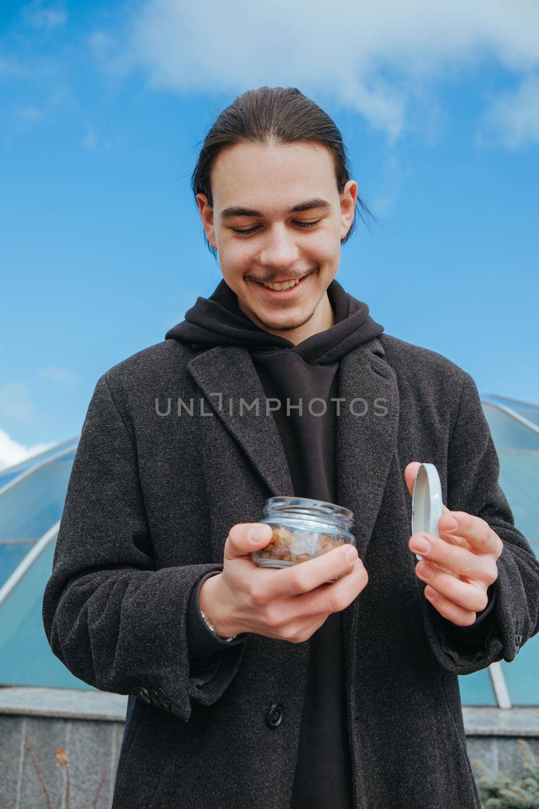 Young gay hipster eating peanuts at the street smiling happy sunglasses by Symonenko