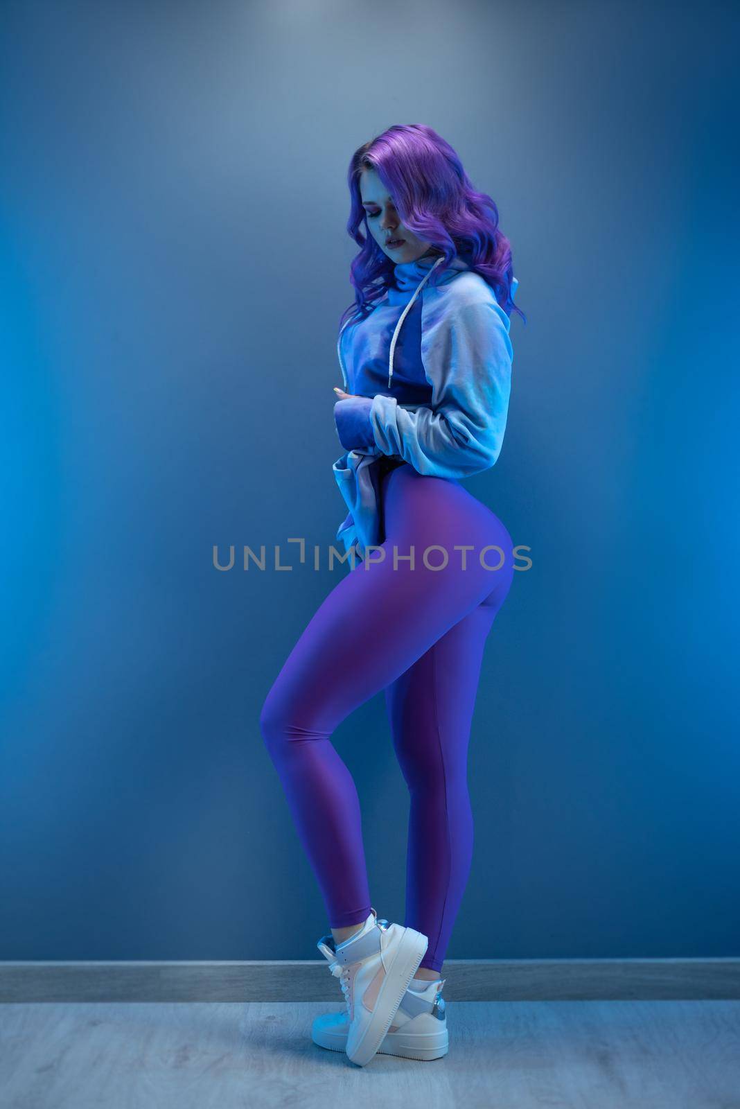 girl in stylish purple sportswear and with purple hair poses sexually