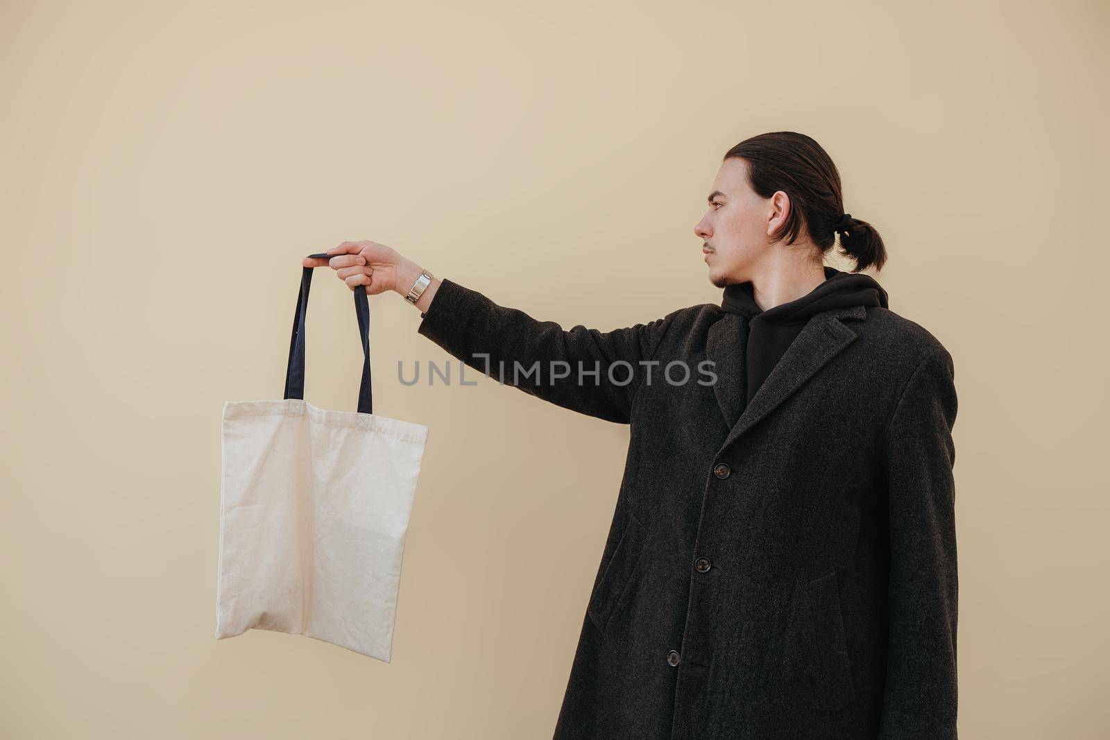 Young man holding textile bag on color background, closeup. Mockup for design hipster