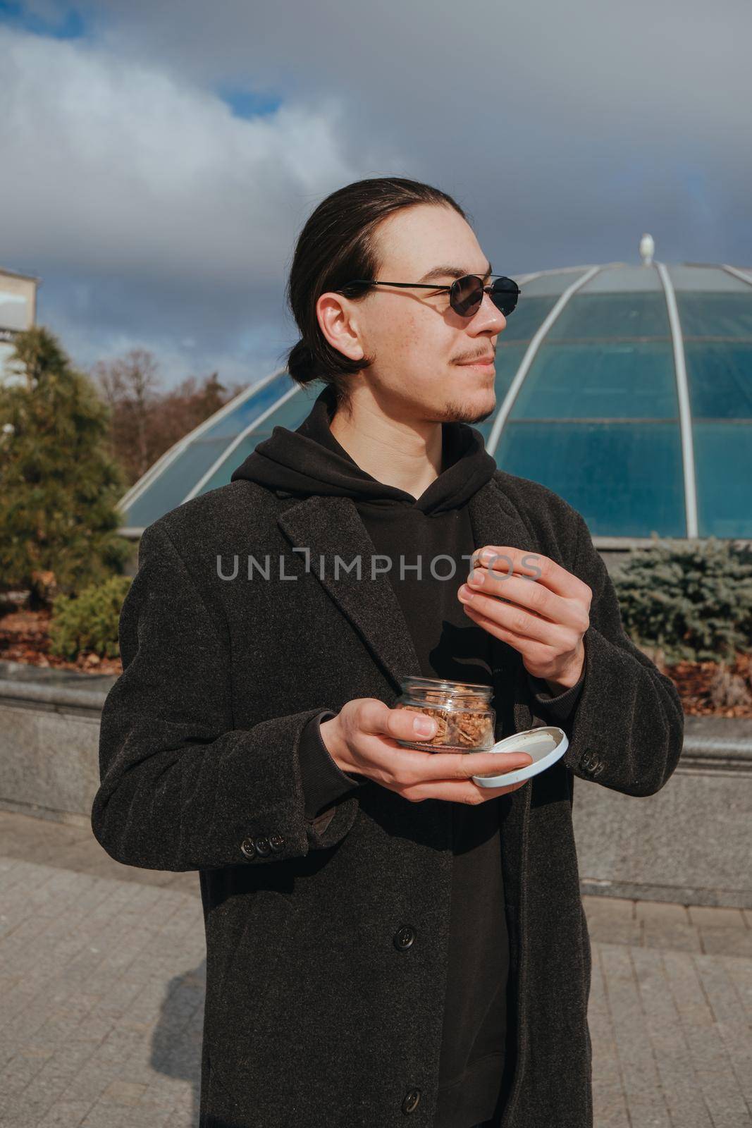 Young gay hipster eating peanuts at the street smiling happy sunglasses. Healthy lifestyle
