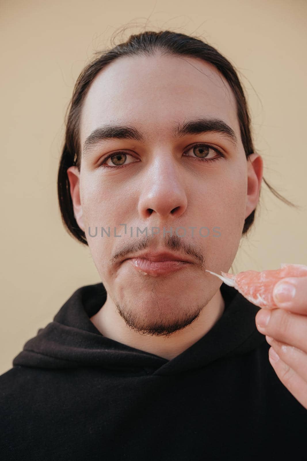 young Caucasian guy bites sour unripe citrus. A man makes a face because of the sour taste of fruit, posing on a green background. Vitamin C. by Symonenko