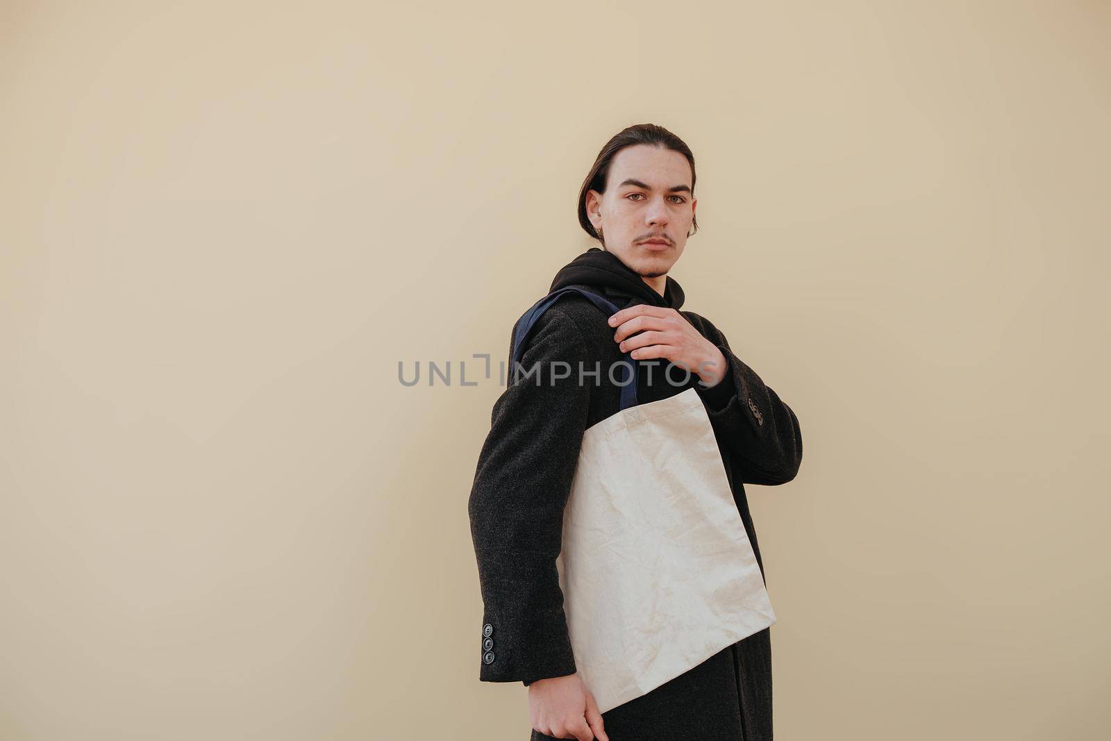 Young man holding textile bag on color background, closeup. Mockup for design hipster