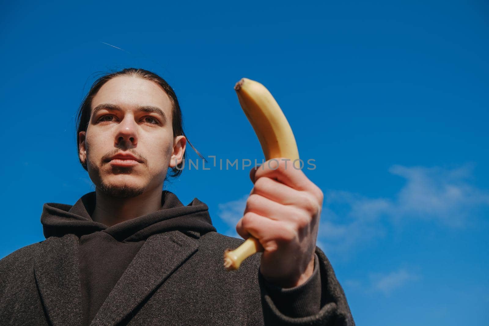killer man with a banana instead of a gun. angry and confident look. Portrait of a nerd with mustache holding a banana weapon in his hand.