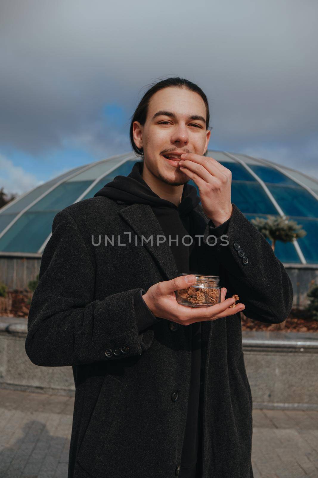 Young gay hipster eating peanuts at the street smiling happy sunglasses. Healthy lifestyle