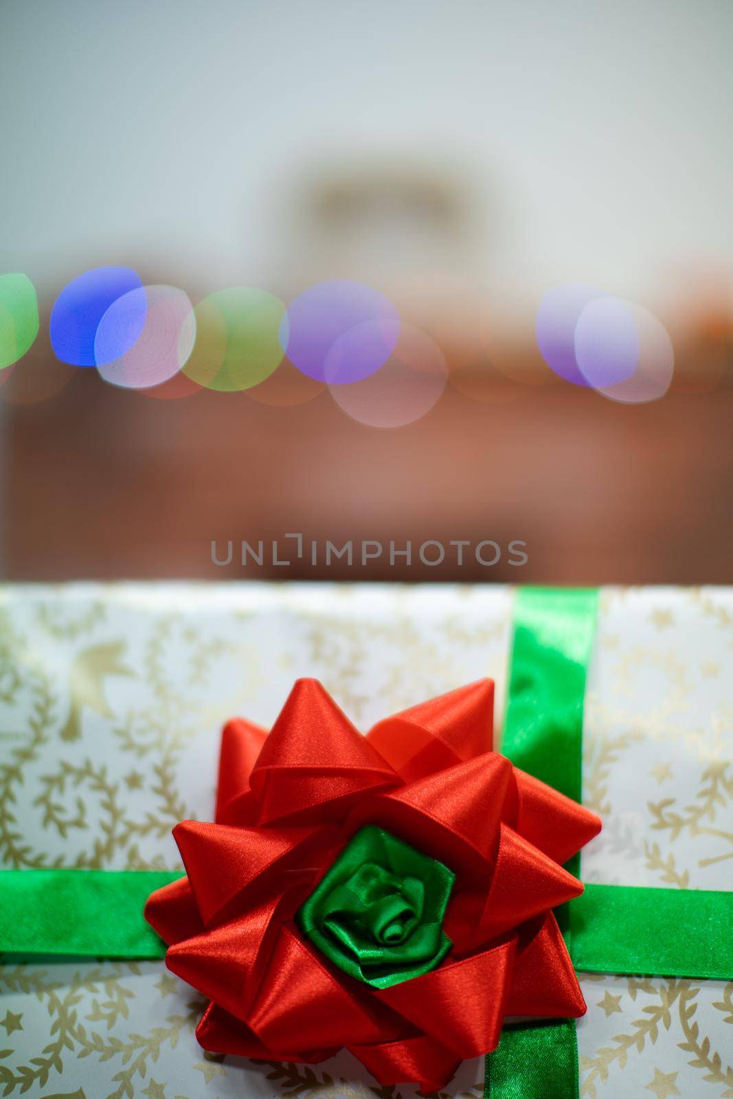 A large red bow on a Christmas gift. A decorative box with a Christmas gift in the background with cork lights.